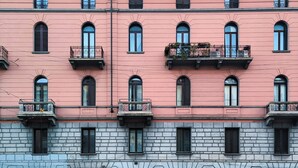A multi-story building with pink and grey stone facades, multiple balconies, and arched windows.