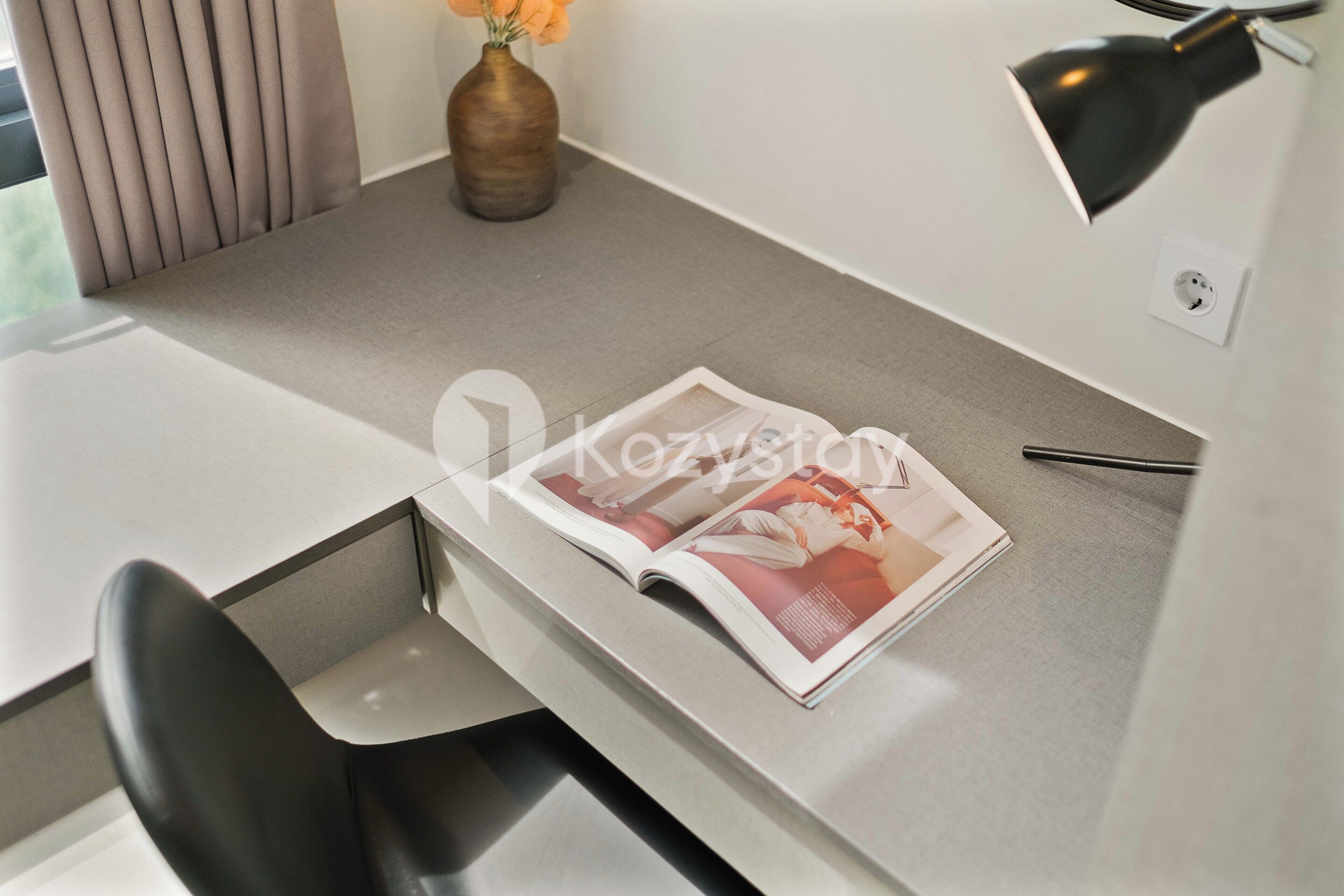 A modern office desk with a magazine, a vase with flowers, and a desk lamp.