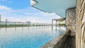 A rooftop infinity pool with a city view, a covered seating area, and a decorative wall.