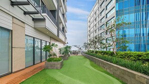 A modern building with a courtyard featuring artificial grass, planters with greenery, and a wooden deck.