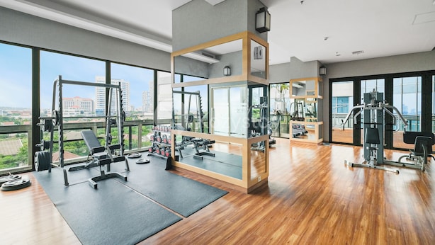 A spacious gym with large windows, various exercise equipment, and a wooden floor.