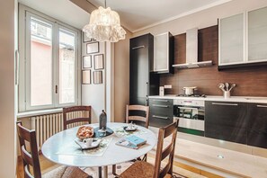 Una cocina moderna con comedor, que incluye una mesa redonda, sillas, una araña y electrodomésticos integrados.