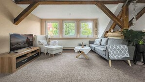 A cozy living room with a TV, white armchair, grey sofa, and a small round table. - Cozy & nature-loving apartment “Lichtblick” (Tschernitz)