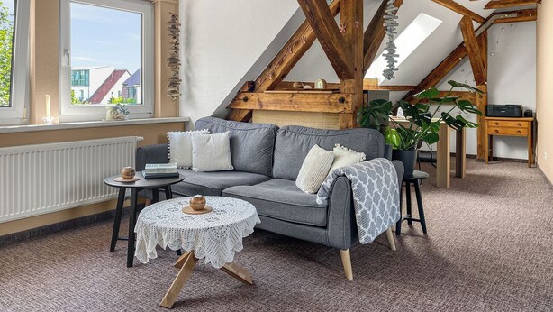 A cozy room with a grey sofa, a small round table, and a wooden desk. - Cozy & nature-loving apartment “Lichtblick” (Tschernitz)