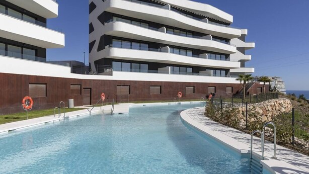 Ein modernes Gebäude mit Pool, mehreren Balkonen und freiem Blick auf das Meer.