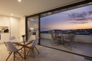 Un intérieur moderne avec un coin repas et un balcon donnant sur une vue panoramique de la ville au crépuscule.