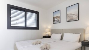 A hotel room with a bed, two bedside tables, a window with blinds, and two framed pictures on the wall.