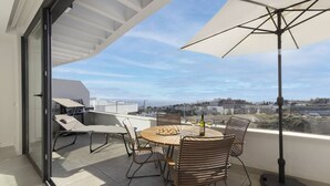 Une terrasse sur le toit, avec une table, des chaises, un barbecue et un grand parasol.