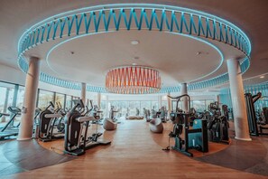 A modern gym with cardio machines, free weights, and a central circular design with a hanging light fixture.