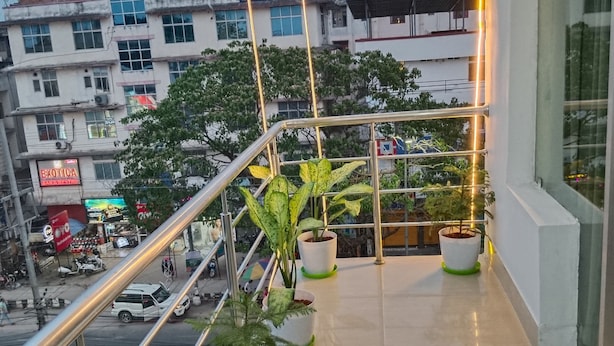 A balcony with potted plants, a metal railing, and a view of a busy street with buildings and shops. - Hotel Pariwar Mahal (Guwahati)