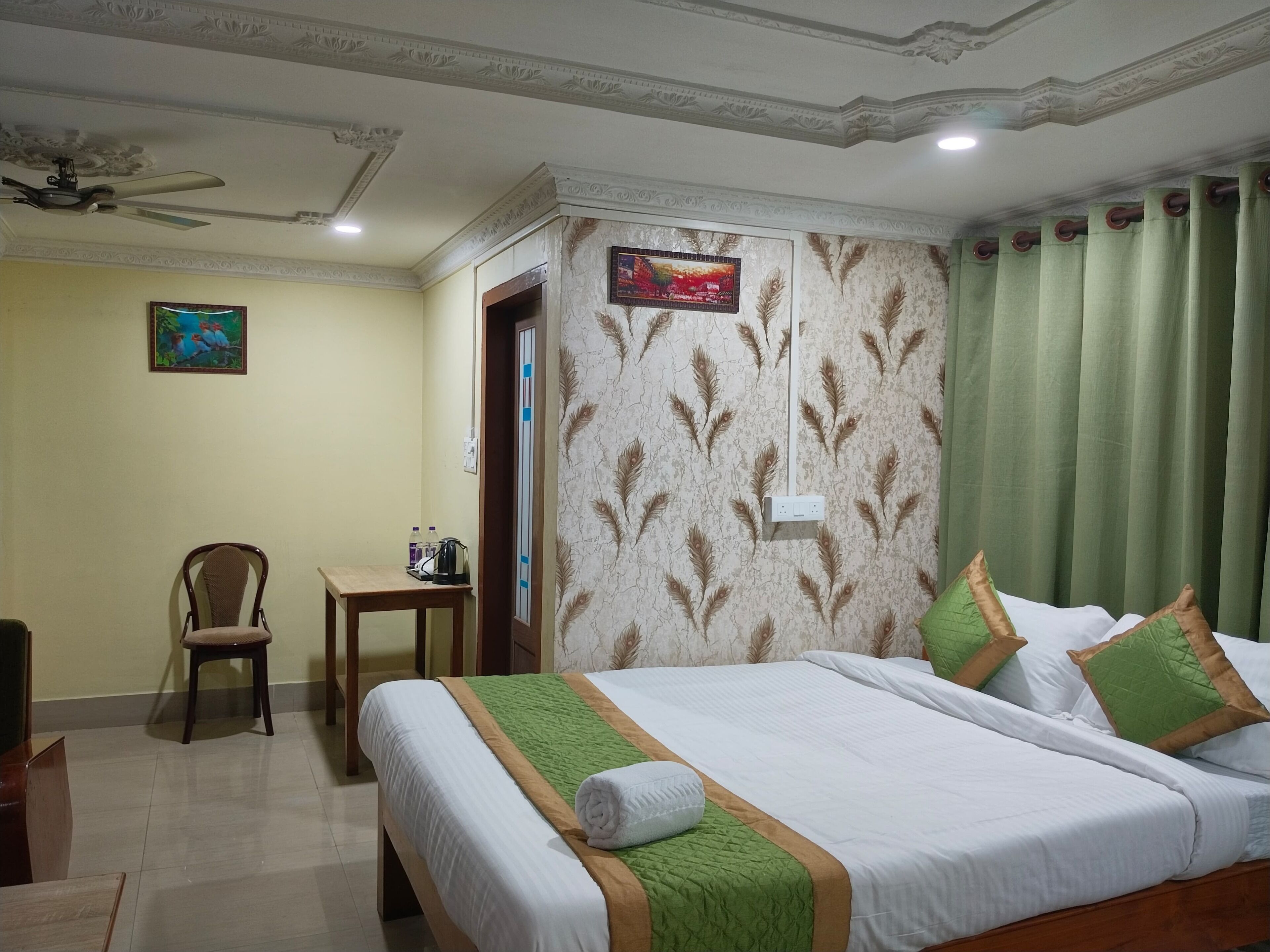 A hotel room with a bed, a chair, a small table, and a painting on the wall.