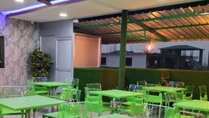 A restaurant with green tables and chairs, a ceiling fan, and a decorative plant. - Hotel Pariwar Mahal (Guwahati)
