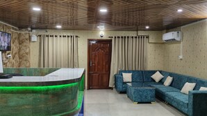 A reception area with a wooden ceiling, a reception desk with green lighting, a blue sofa with cushions, and a wooden door. - Hotel Pariwar Mahal (Guwahati)