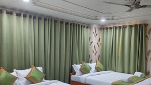 A hotel room with two beds, green curtains, and a ceiling fan. - Hotel Pariwar Mahal (Guwahati)