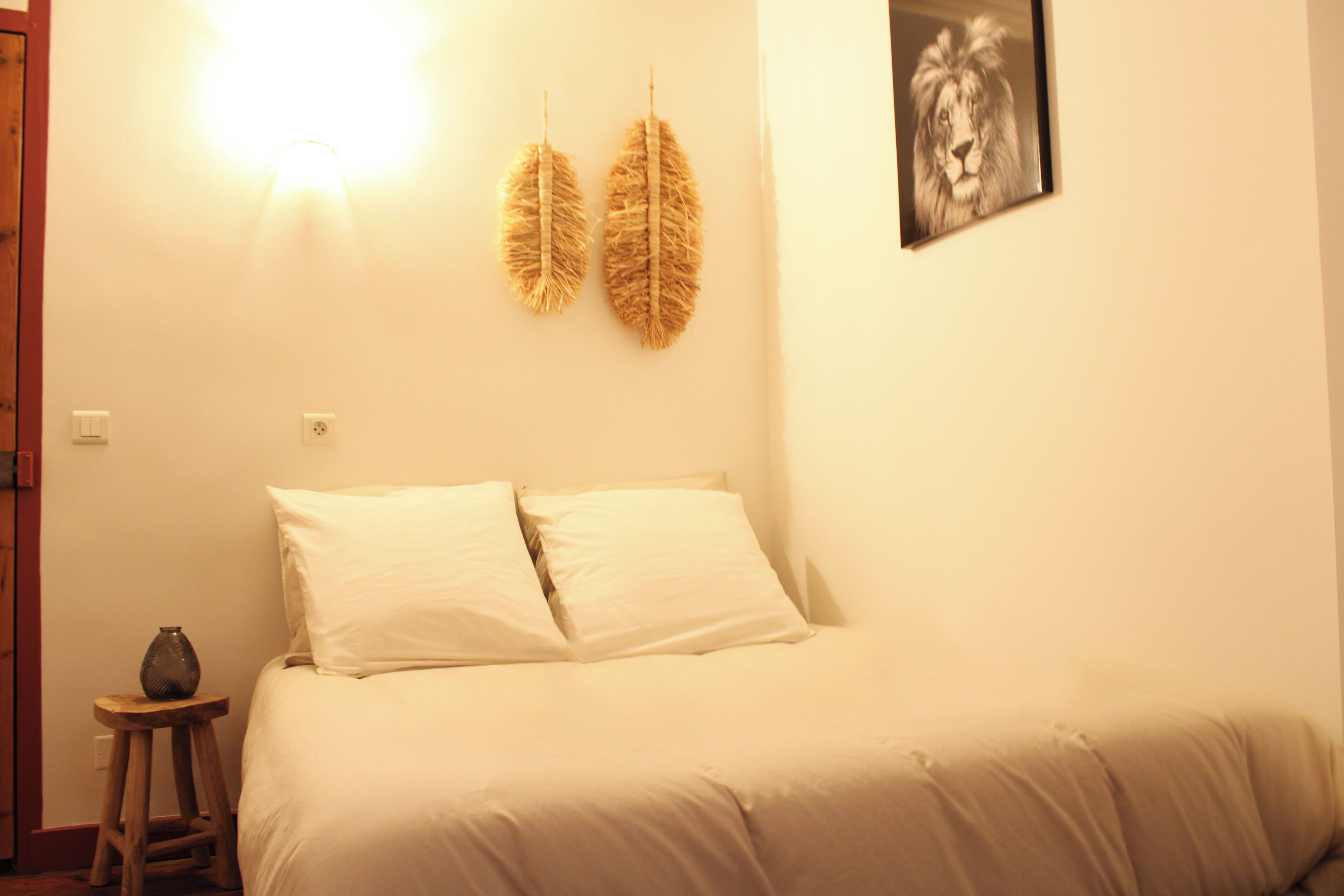 Une chambre à coucher avec un lit, deux oreillers, une table de chevet, un vase et un tableau accroché au mur.