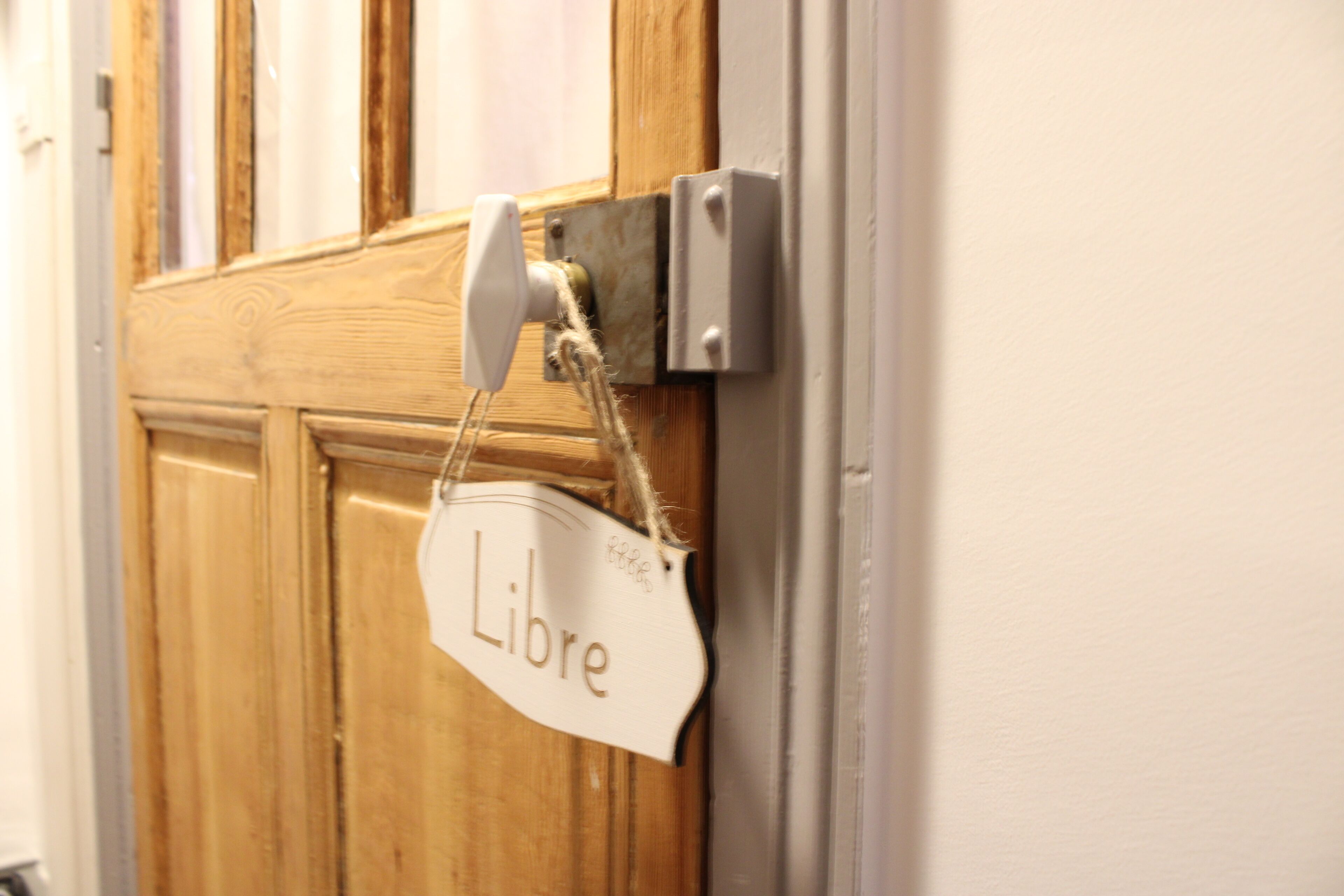 A wooden door with a white sign hanging on a metal hook that reads "Libre".