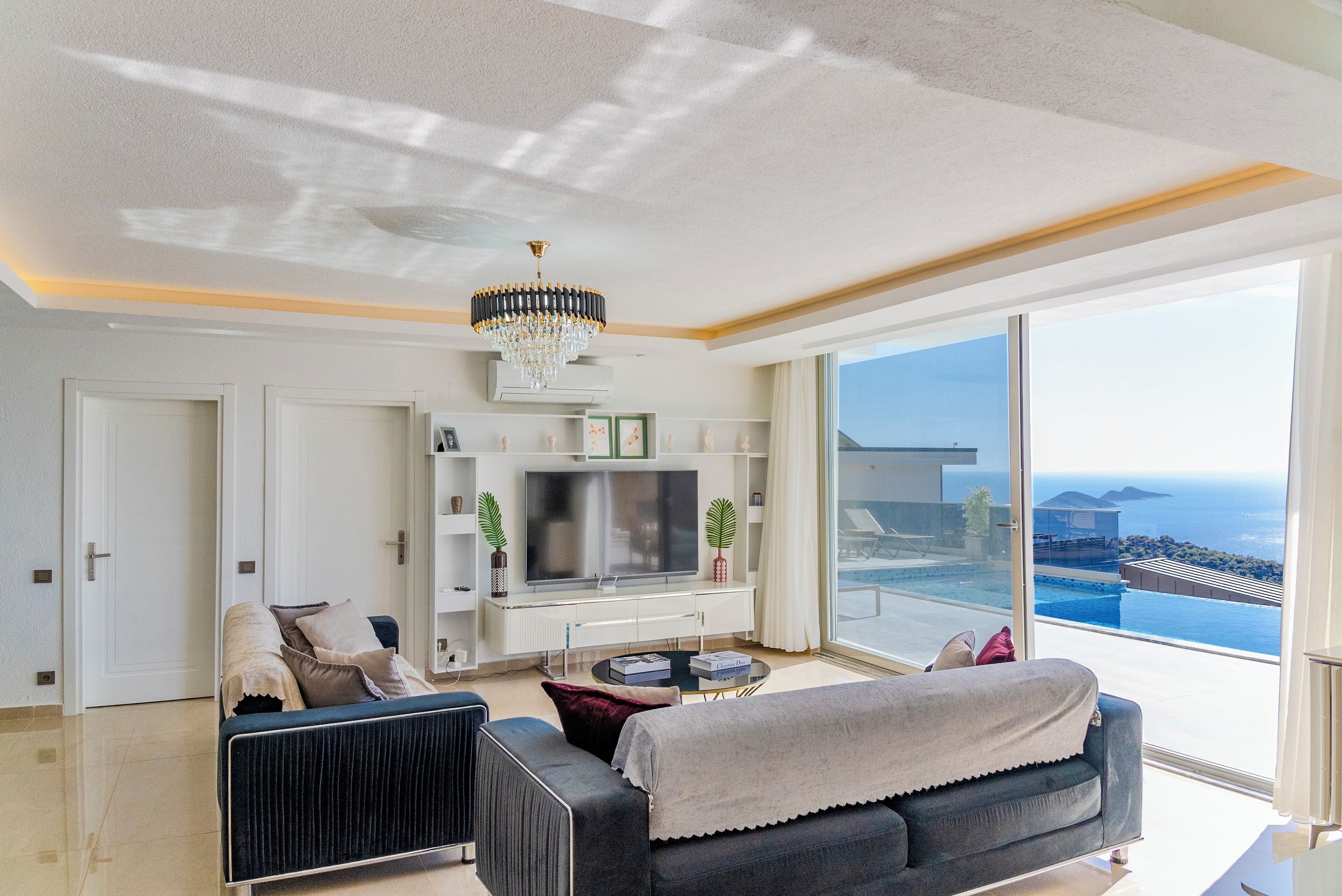 A modern living room with a large TV, comfortable seating, and a view of the ocean.
