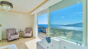 Un baño moderno con una bañera grande, una araña y vista al mar.