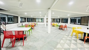 Un amplio comedor interior con varias mesas y sillas, ventanas grandes y ventiladores de techo.