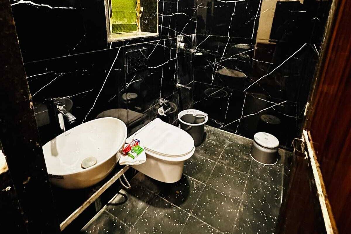 Un baño pequeño y funcional con lavamanos, inodoro y zona de ducha, con azulejos de mármol negro y un ventanal.