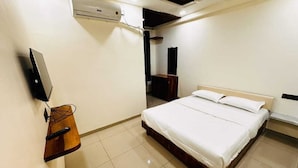 Un dormitorio con una cama, un televisor fijado a la pared y una mesita de noche de madera.