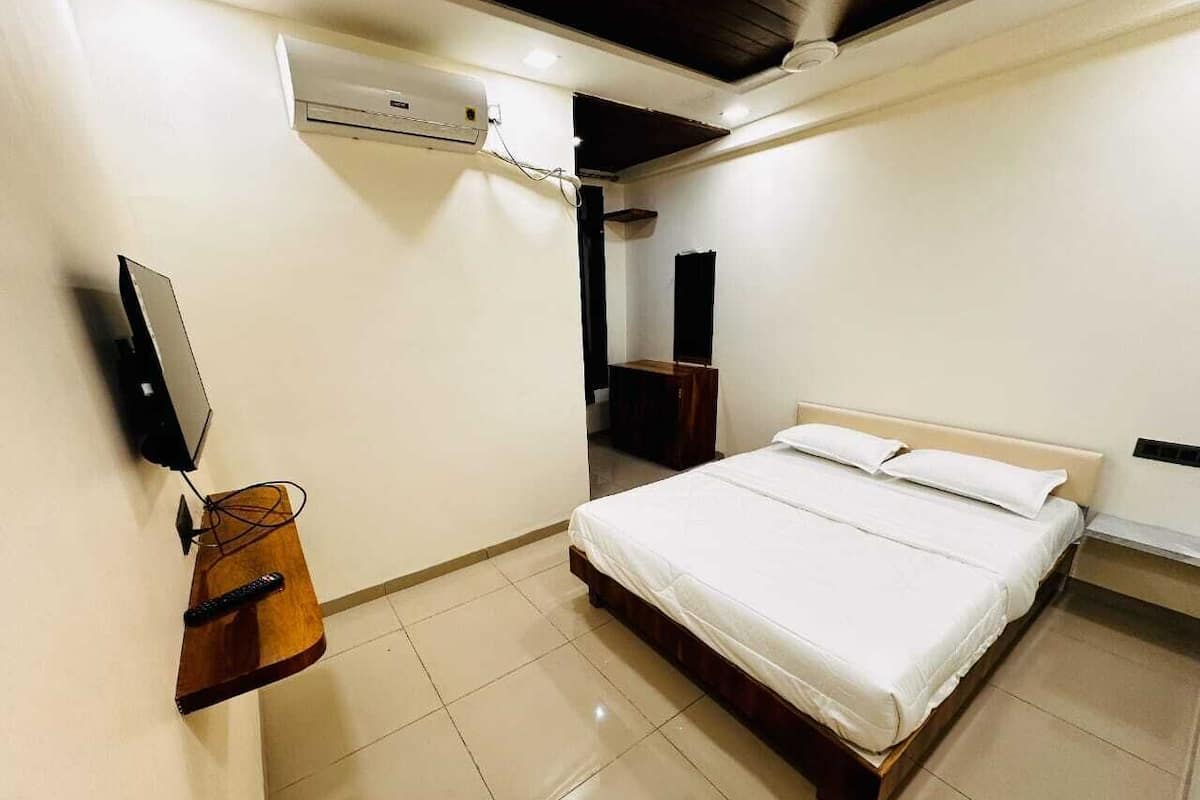 Un dormitorio con una cama, un televisor fijado a la pared y una mesita de noche de madera.