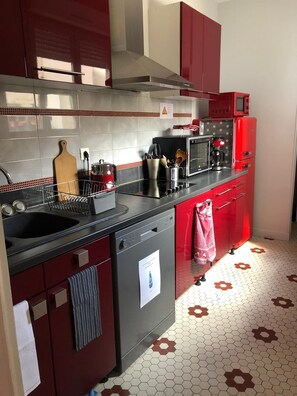 A kitchen with red cabinets, a black countertop, a microwave, and a coffee maker. - Le Rameau 4 room ground floor apartment Sainte Ménéhould town center Marne (Sainte Ménéhould)