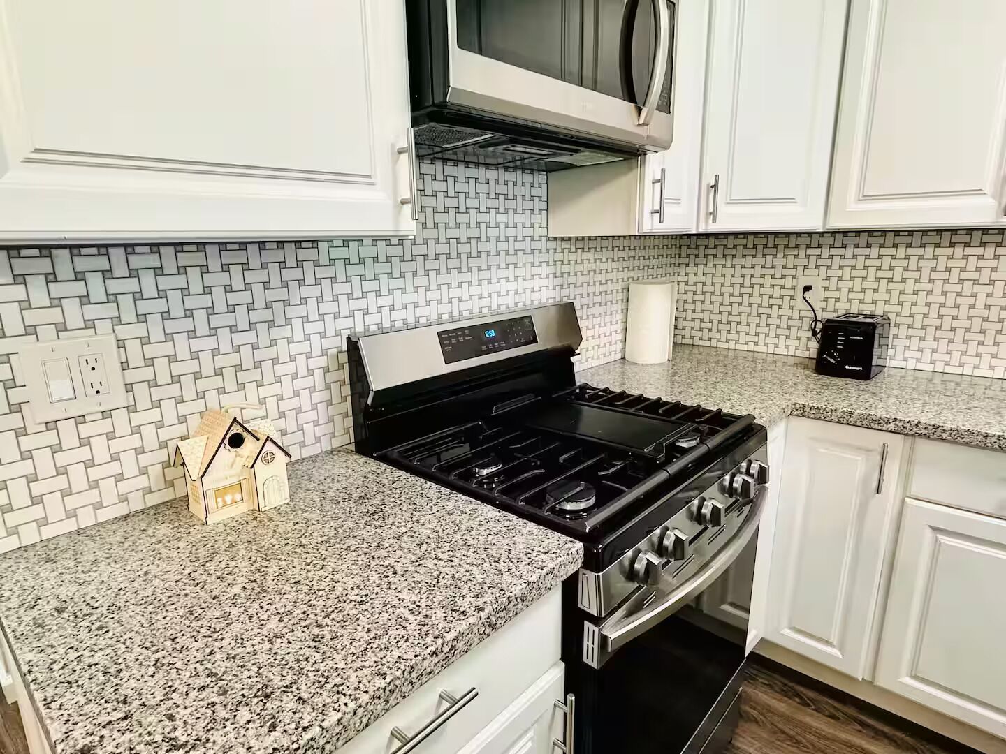 Una cocina con armarios blancos, encimera de granito, estufa, horno, microondas y tostadora.