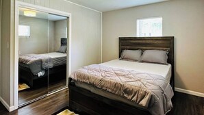 Ein Schlafzimmer mit Bett, Spiegel, Fenster und Deckenleuchte.