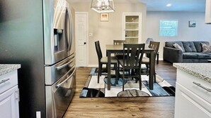 Una cocina moderna con un refrigerador de acero inoxidable, un comedor con mesa y sillas, y un sofá gris en la sala.