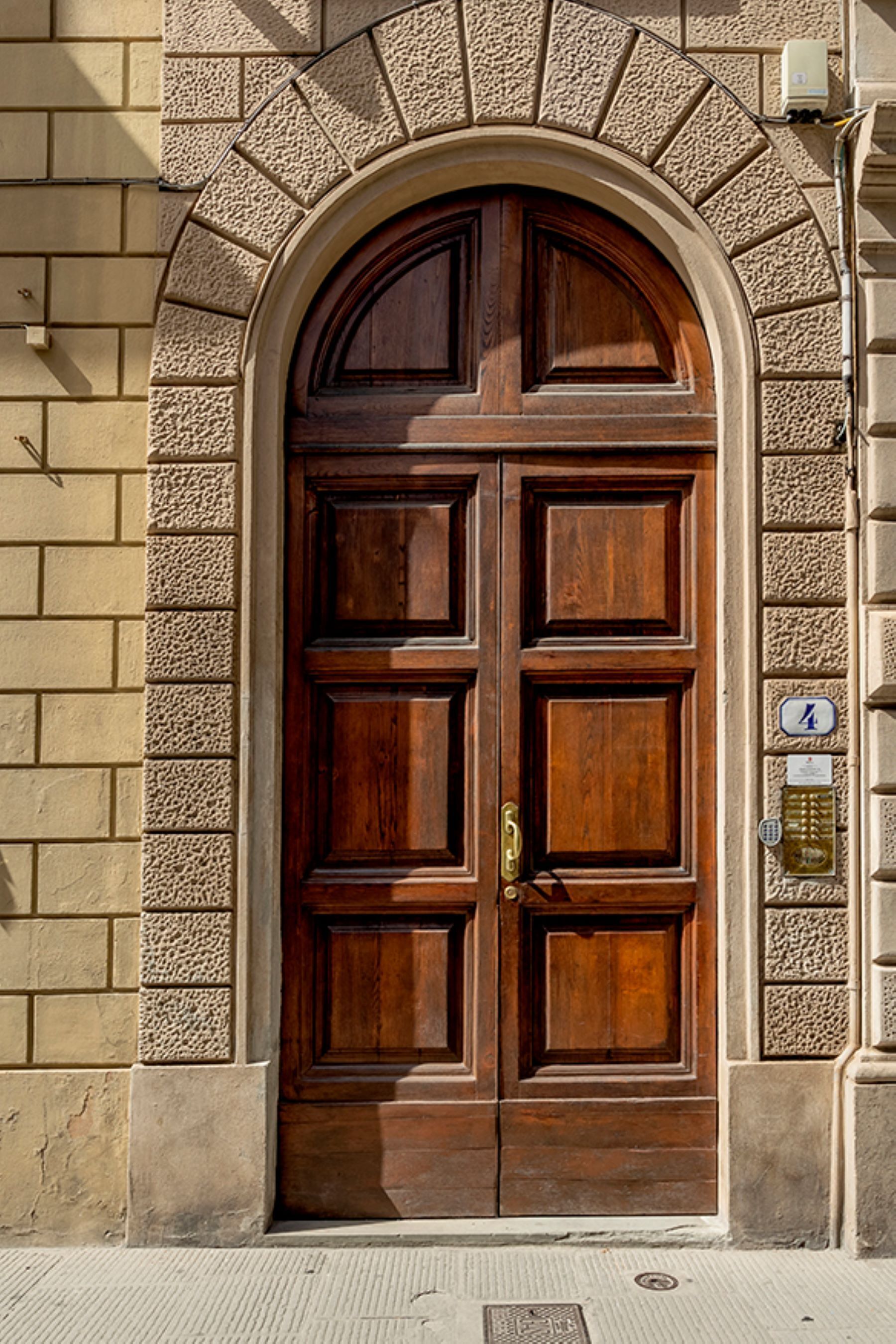 A large wooden door with a stone archway, a brass door knocker, and a mailbox on the wall.