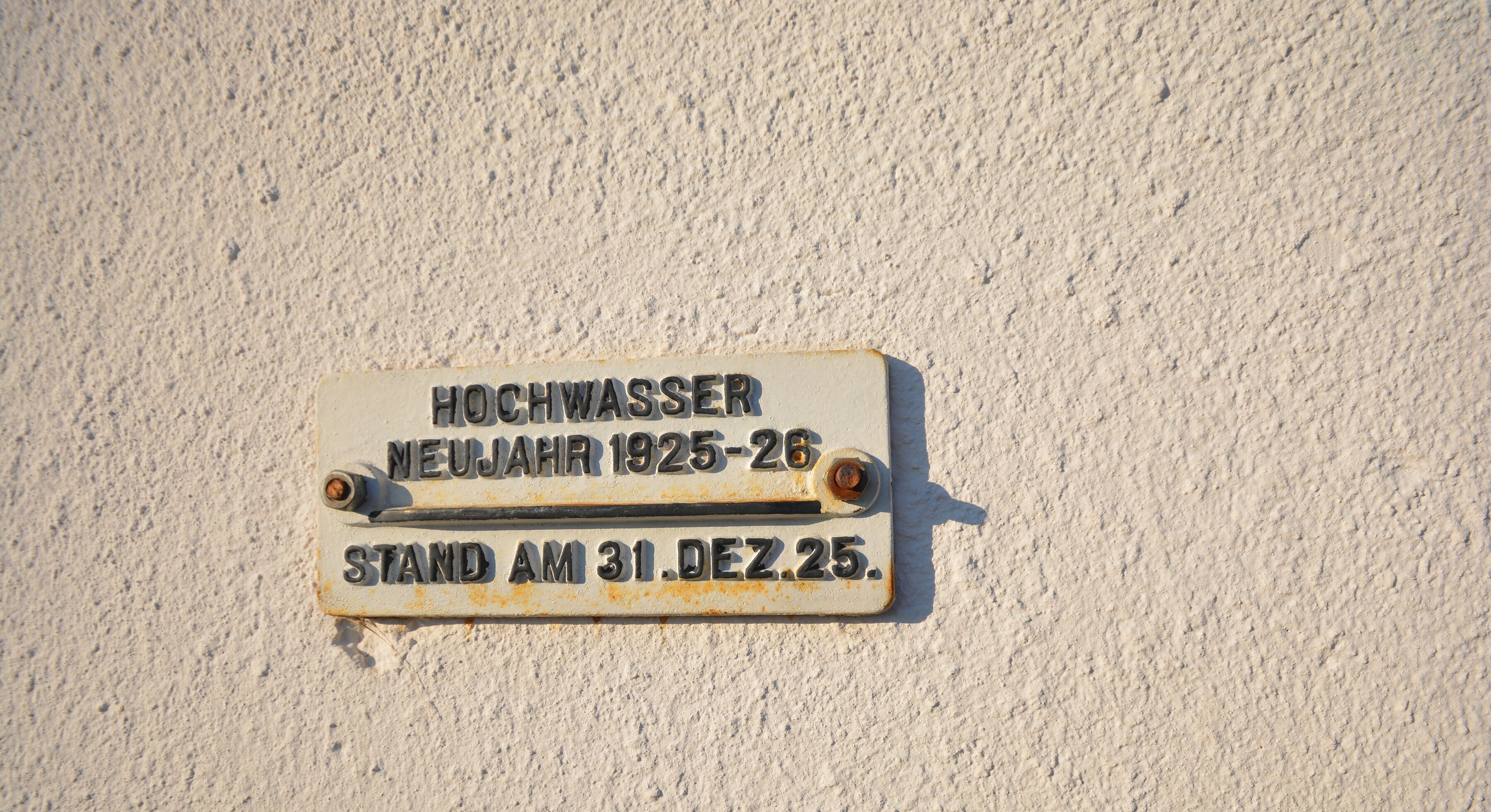 A weathered metal plaque on a textured wall with inscriptions in German.