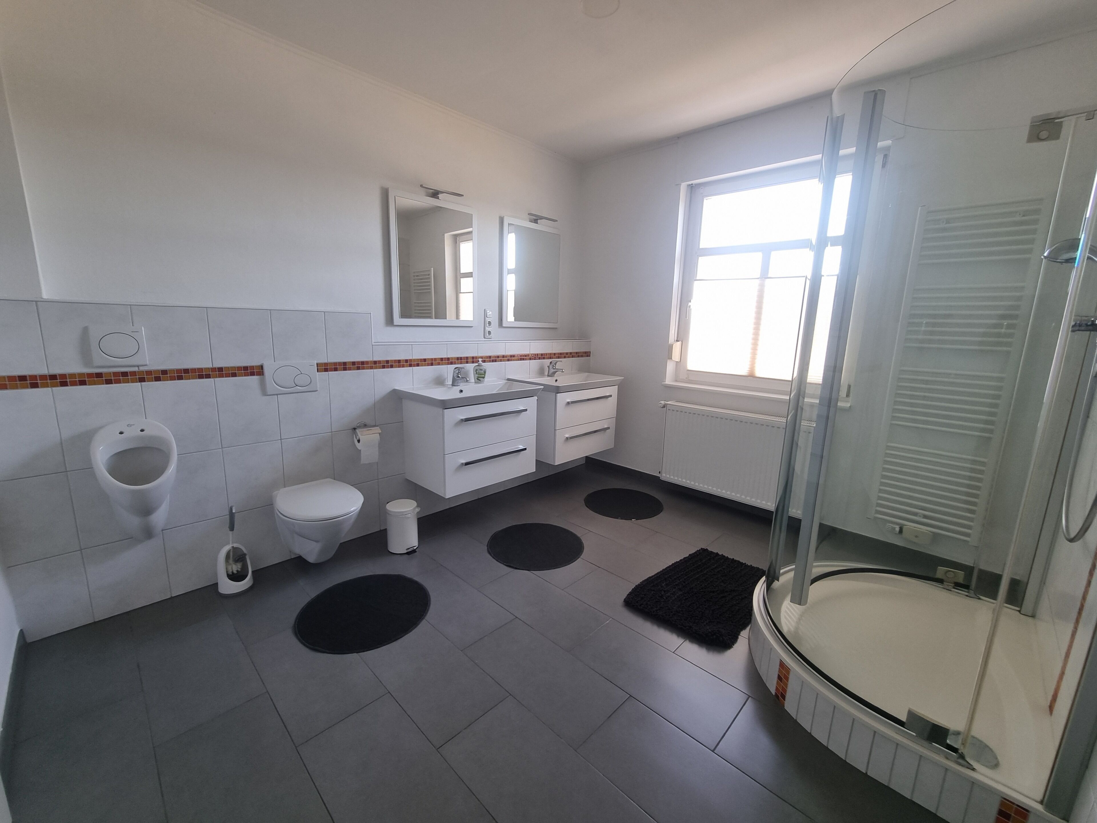 A bathroom with a toilet, urinal, sink, mirror, and shower.