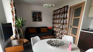 Una sala de estar moderna con una mesa redonda blanca, dos sillas blancas, un sofá, un televisor y una planta en maceta.