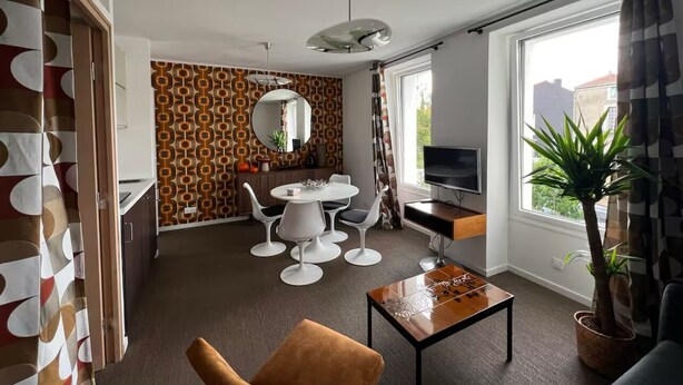 Una sala de estar moderna con comedor, televisor y un amplio ventanal con cortinas.