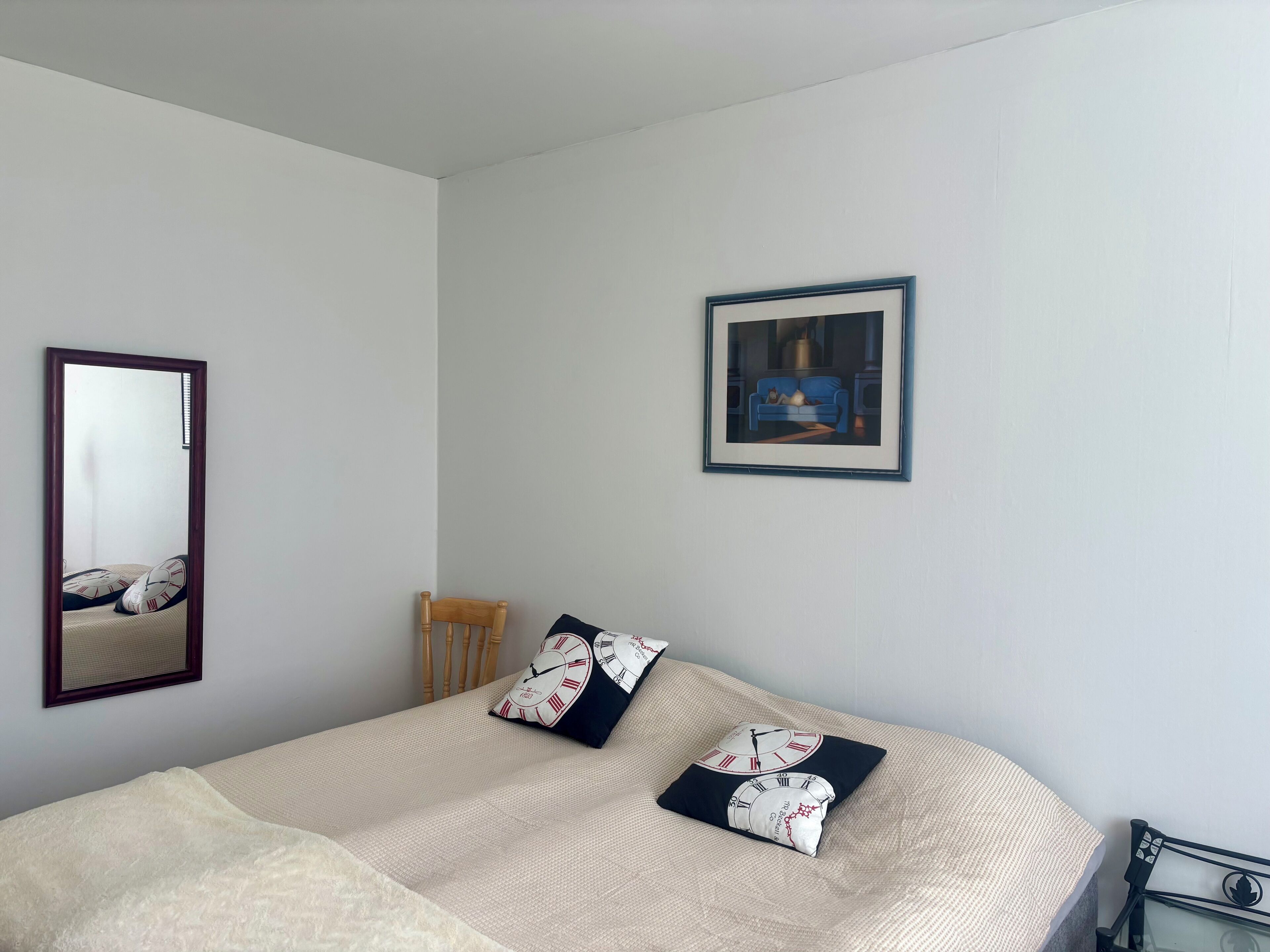 Ein Schlafzimmer mit einem Bett, einem Sessel, einem Spiegel und einem gerahmten Bild an der Wand.