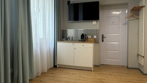 Uma cozinha com piso de madeira, um armário branco, uma TV preta montada acima do balcão e uma porta branca.