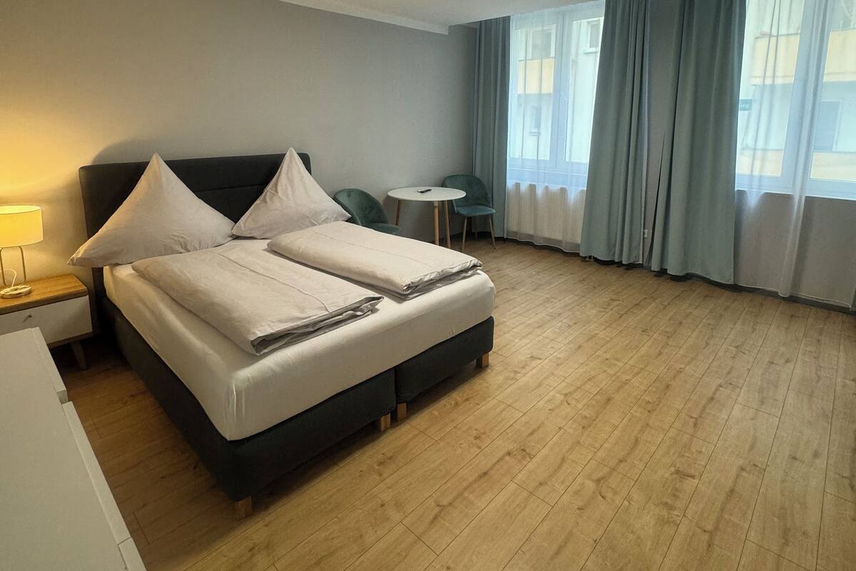 Une chambre d’hôtel avec un lit, une table de chevet, une lampe et une petite table ronde accompagnée d’une chaise.
