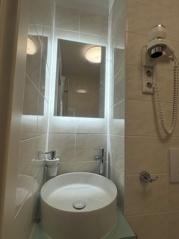 A bathroom with a sink, mirror, and a wall-mounted hairdryer.