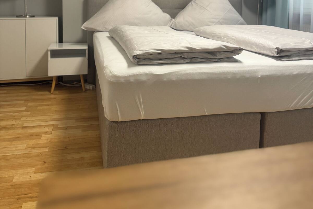 Un lit bien fait, avec des oreillers, une table de chevet avec une lampe et une petite table d’appoint.