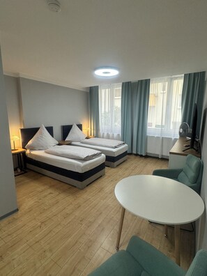 A hotel room with two beds, a round table, a chair, a TV, and a window with curtains.
