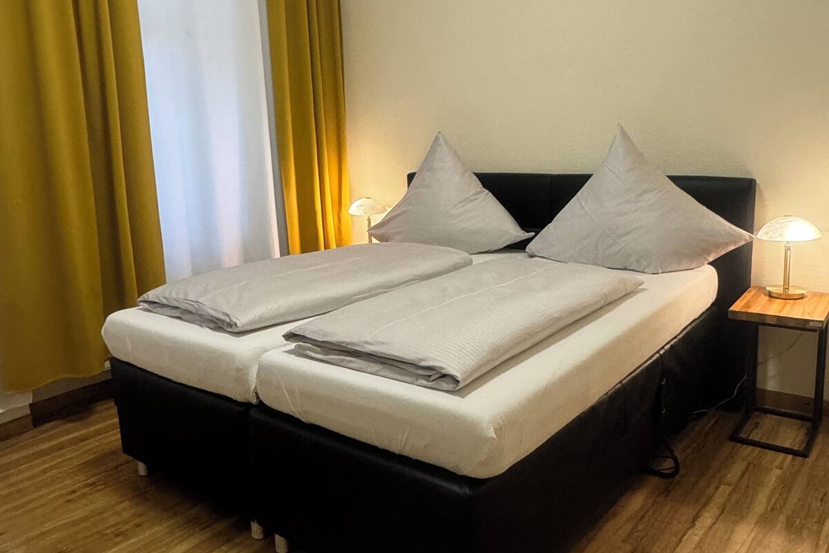Un lit double avec deux oreillers, une table de chevet avec une lampe et une fenêtre avec des rideaux.
