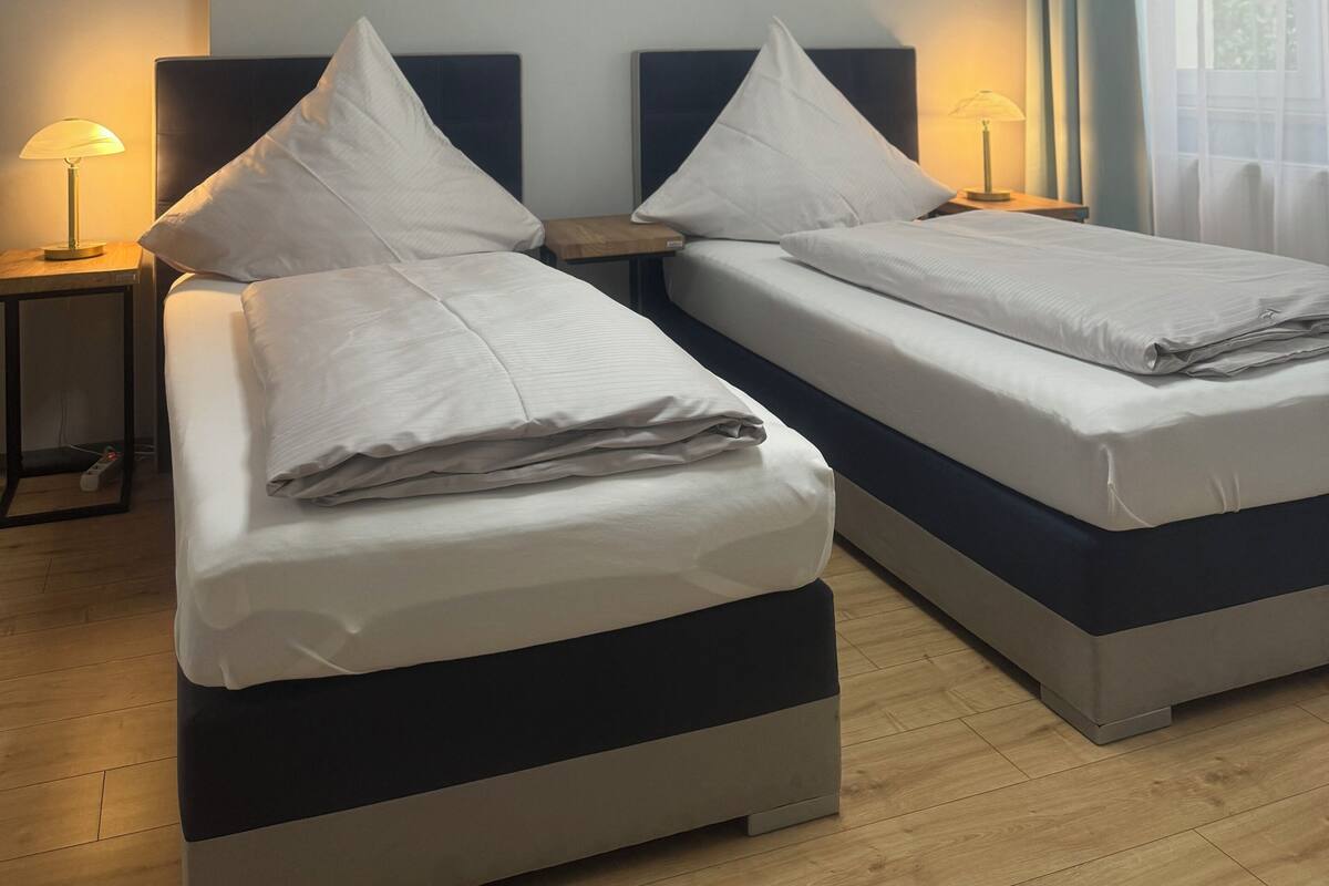 Une chambre d’hôtel avec deux lits, un luminaire au plafond et une fenêtre avec des rideaux.