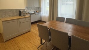 Cozinha compacta com mesa e cadeiras, forno embutido e janela com cortinas.