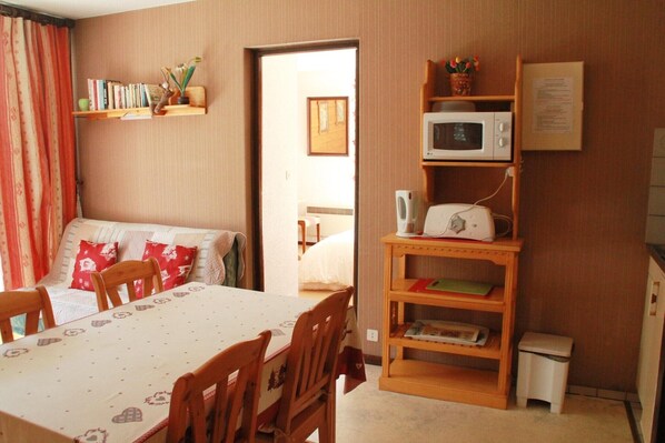 A cozy room with a bed, a dining table, chairs, a bookshelf, a microwave, and a small trash bin. - Apartment in Chatel with balcony (Châtel)