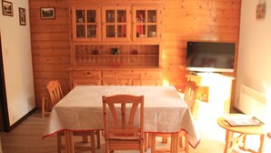 Puisesti sisustettu ruokasali, jossa on ruokapöytä ja -tuoleja, lasiovilla varustettu kaappi ja televisio.