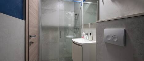 Un baño moderno con ducha envuelta en vidrio, un lavamanos blanco y un perchero para toallas.