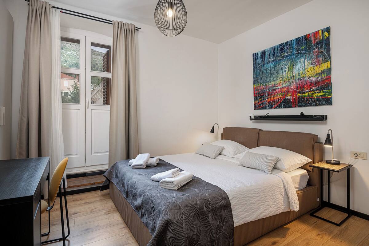 Un dormitorio ordenado con cama, mesita de noche y escritorio.
