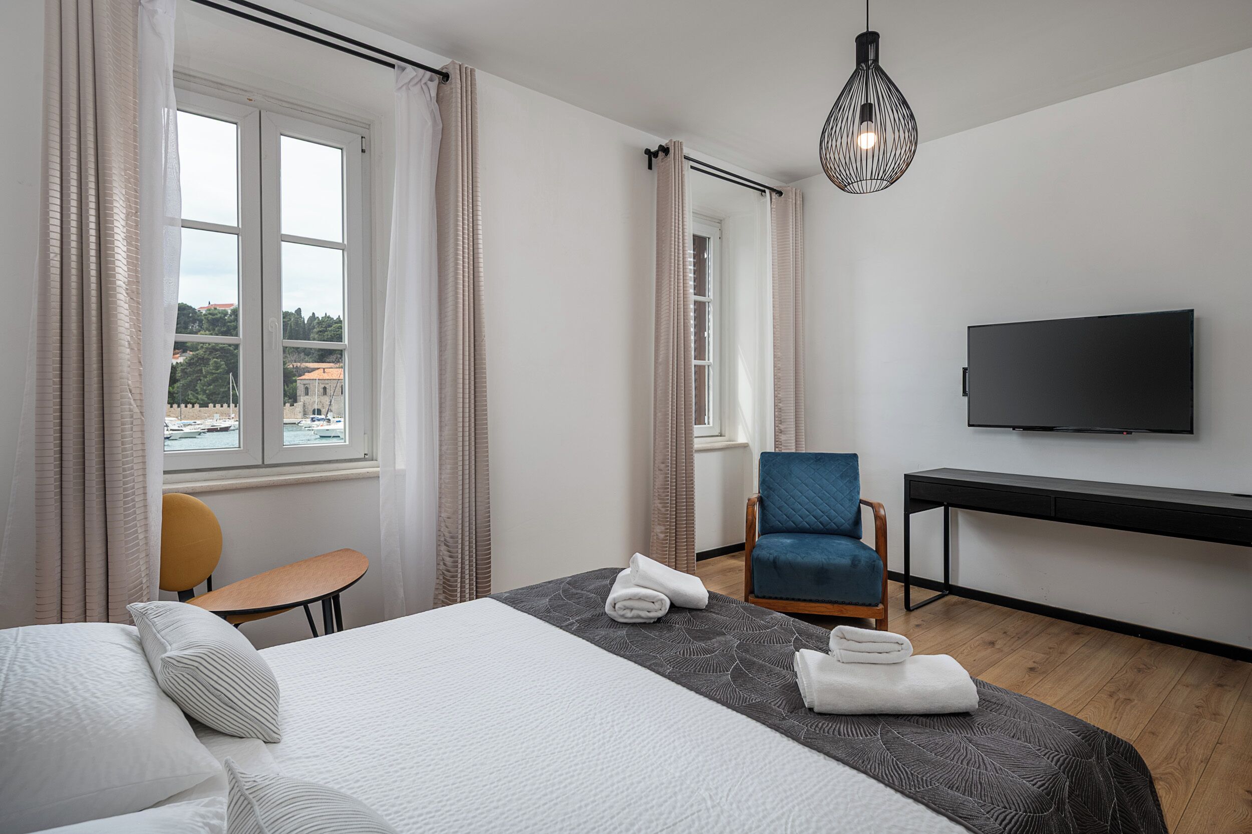 A modern hotel room with a large bed, a desk, a chair, and a TV.