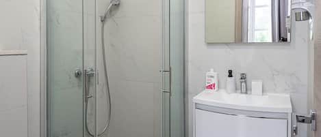 Un baño moderno con ducha de vidrio, un lavabo blanco y un inodoro.